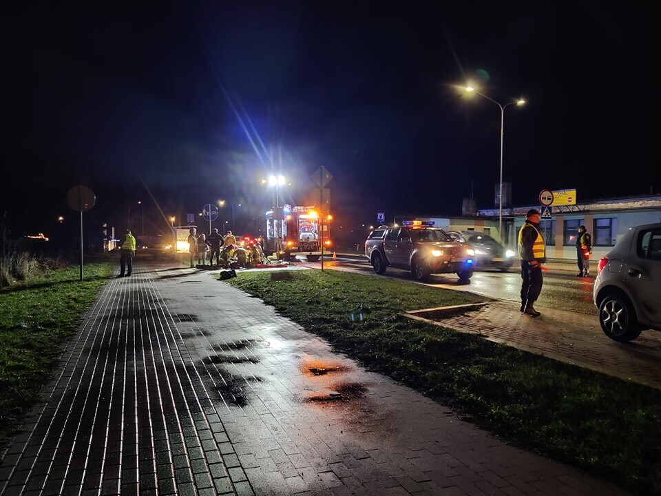 Służby straży pożarnej i straży miejskiej zajmują się potrąconym rowerzystą nad którym klęczy kilku strażaków